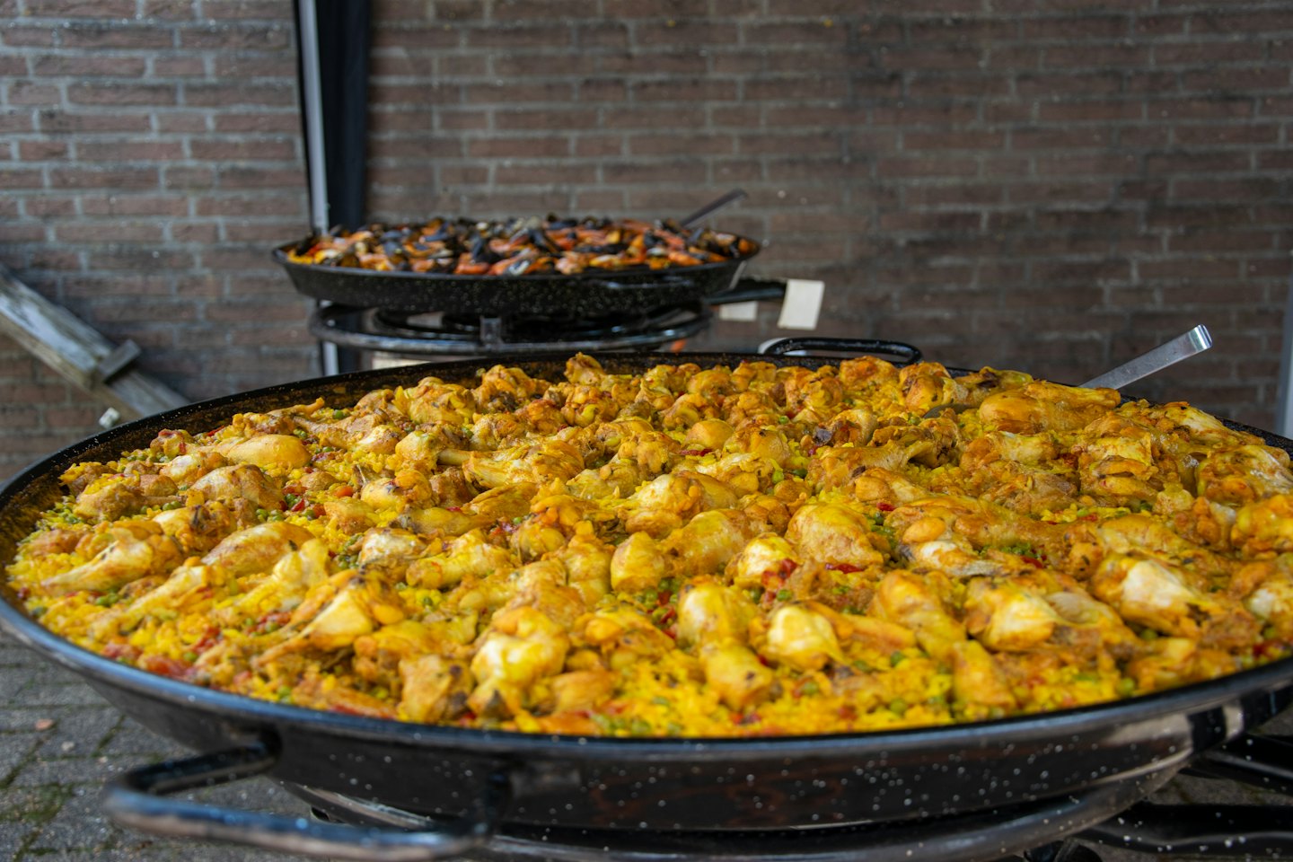 Due grandi padelle di paella che cuociono paella all'aperto su un muro di mattoni.