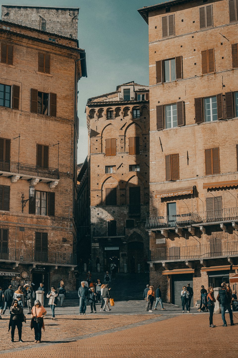 Persone che passeggiano in una storica piazza europea con edifici antichi.