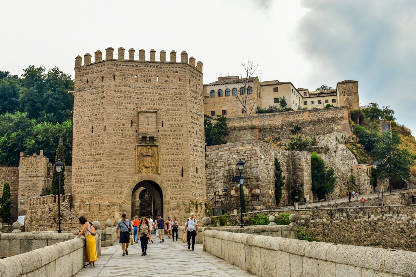 Turisti attraversano un ponte di pietra verso una torre porta medievale.